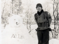 (December 1942) “Note fingers sticking out of my pockets are my gloves, and on the snow bear reads ALOHA.” Eugene Kawakami is standing in the snow wearing his G-I glasses and muffler made for him by his wife, Gladys.  [Courtesy of Joanne Kai]