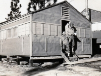 (September 1942) S/Sgt. Gora & I at the doorway of our home in Camp Shelby, Mississippi. The picture was taken on a cold day, so we have the shutters down. Eugene Kawakami is pictured on the left.  [Courtesy of Joanne Kai]