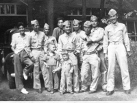 7 soldiers in dress uniform with young children in front of a car and building [Courtesy of Leslie Taniyama] Inscription: Reverse: At Journey’s End. Devil’s Lake, Wisconsin, July 4, 1942