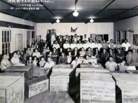 Thomas Higa and wife, Toshiko, are pictured in front center. Photo was taken after packing relief supplies for the victims of the Battle of Okinawa, at the Wailuku Showa Seinen Kaikan (Wailuku Showa Youth Association Hall). Donation crates were sent from Maui to be collected by the Okinawa Clothing Relief Committee at Club 100. (December 15, 1945) [Courtesy of: Thomas Taro Higa Family Collection]