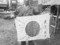 Tom Matsumura holds an enemy sword and flag while stationed in the Philippines. [Courtesy of Florence Matsumura]