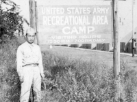 Tom Matsumura stands in front of a sign at Camp McCoy, Wisconsin. [Courtesy of Florence Matsumura]