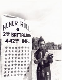 Protestant Chaplain Hiro Higuchi, Waipahu, Oahu, T.H., reads the names on the roll; each name represented by a star on the banner by which he stands.  These 71 men represent the deaths in the 2nd battalion, 442 Infantry, made up of Americans of Japanese descent, that went into action in Italy, June 26, 1944. [U.S. Army Signal Corps]